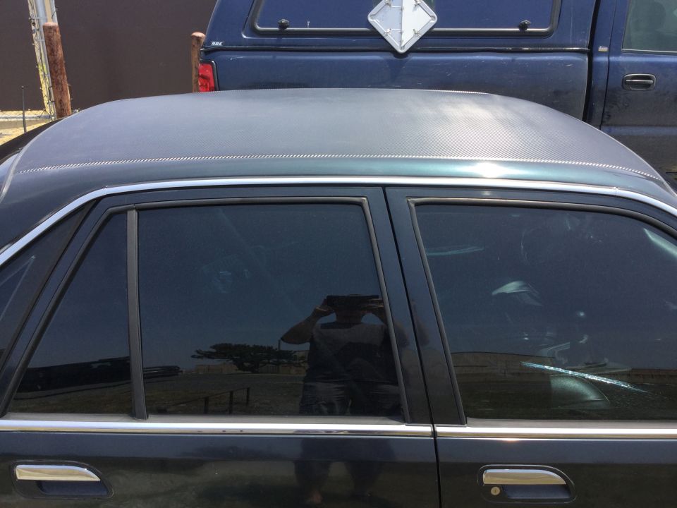 Side view of a dark sedan with tinted windows, a blue pickup truck is behind it