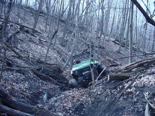 Green off-road vehicle navigating a steep, wooded incline