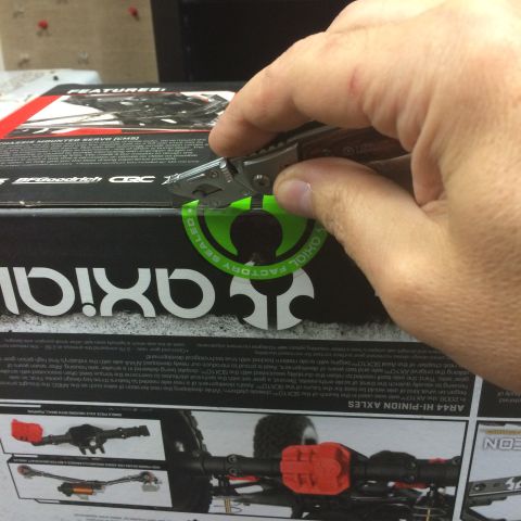 1989 Ford Bronco - A hand uses a utility knife to cut the factory seal on a box for an Axial SCX10 II RC car.
