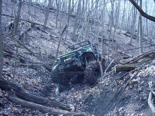 Off-road vehicle with large tires navigating a muddy, wooded hillside