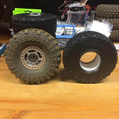 1989 Ford Bronco - A close-up view of two RC car tires, one appearing used and the other new, resting on a wooden table.