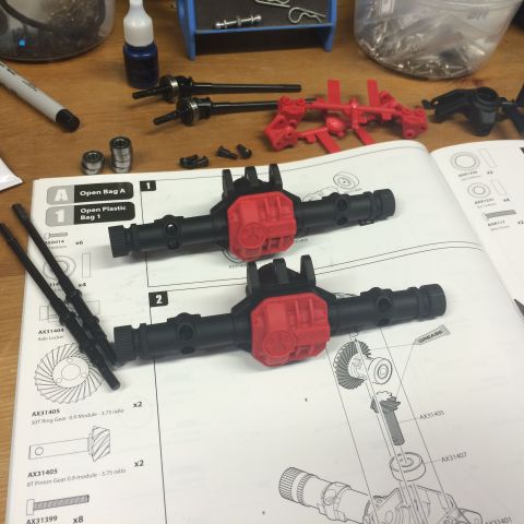 1989 Ford Bronco - Model vehicle axles and an instruction manual are laid out on a wooden surface, with various parts and tools scattered around.