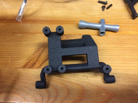 1989 Ford Bronco - A black plastic part for an RC car is shown on a wooden surface with tools and screws.