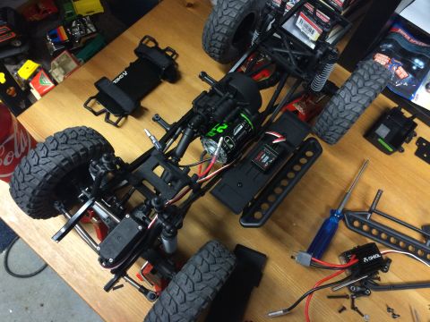 1989 Ford Bronco - The chassis of a remote-controlled car is disassembled on a wooden surface, with various parts scattered around.