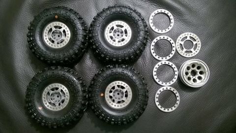 1989 Ford Bronco - A set of four off-road tires and wheels, including separate beadlock rings, are laid out on a dark surface.