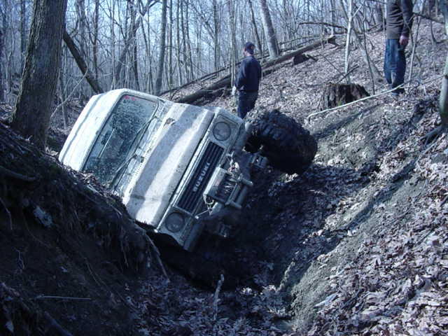 Suzuki Samurai tipped on its side in a ditch with two people standing nearby