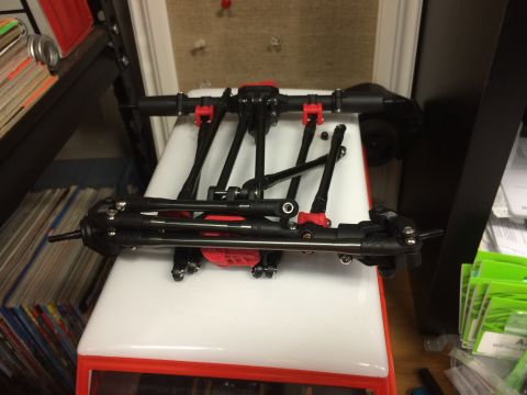 1989 Ford Bronco - Close-up of an RC car's front axle assembly, black metal and red plastic components.