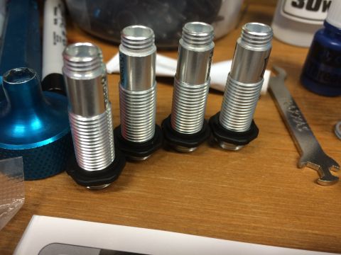 1989 Ford Bronco - Four threaded aluminum shock absorbers for an RC car are laid out on a wooden surface.