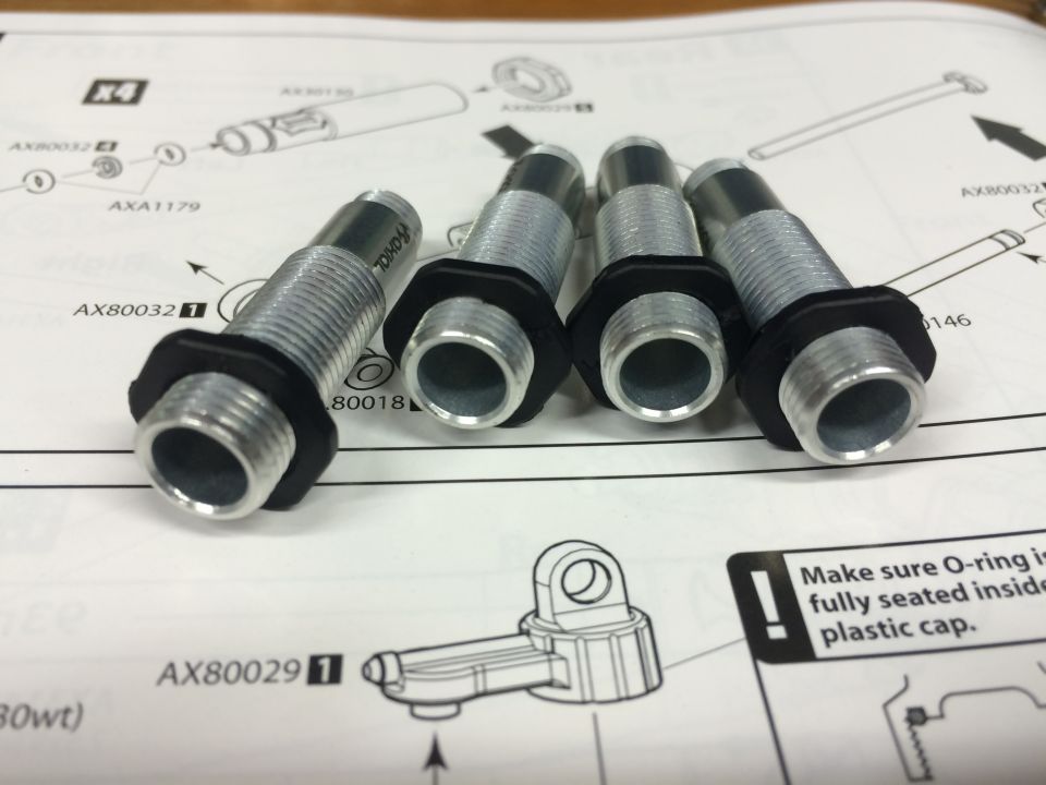 Four metal threaded parts with black rubber gaskets sit on top of an instruction manual with diagrams