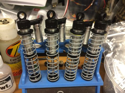 1989 Ford Bronco - A collection of four shock absorbers are organized on a blue stand, with bottles of silicone fluid nearby.