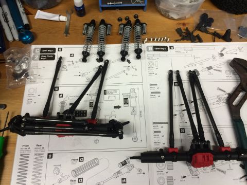 1989 Ford Bronco - RC car suspension parts and assembly instructions are spread across a wooden surface.