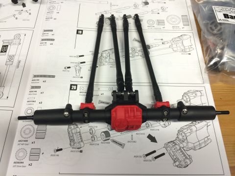 1989 Ford Bronco - An unassembled RC car axle assembly with drive shafts and differential housing rests on assembly instructions.