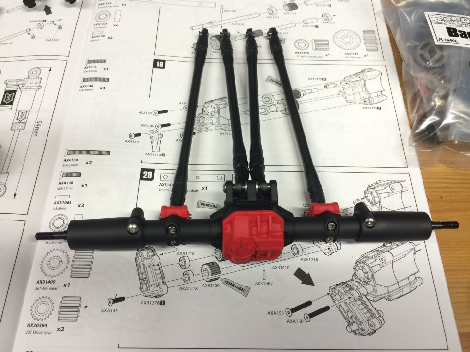 RC car axle assembly with four black drive shafts connected to a red differential housing, laid out on instruction manual pages