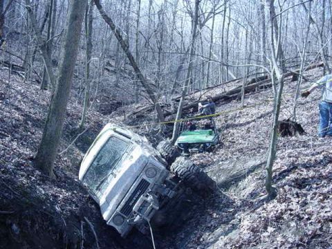1992 Ford Bronco - Two off-road vehicles are stuck in a steep, wooded ditch.