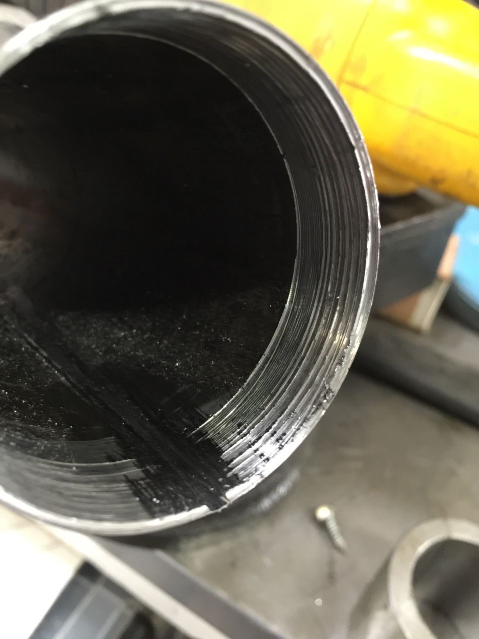 Close-up of the inside of a metal pipe showing significant wear and scoring on the inner surface. A small screw is visible on the surface below