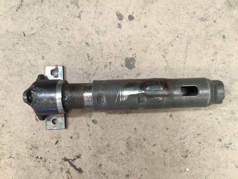 1965 Ford Mustang - A metal driveshaft component with a U-joint and mounting brackets is shown against a concrete background.