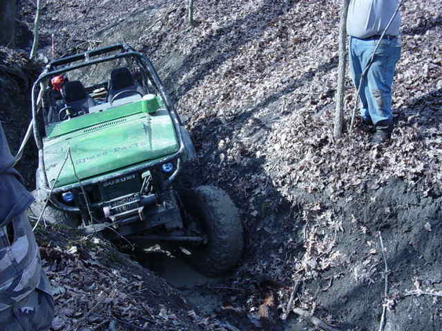 Green off-road vehicle stuck in mud, Suzuki badge visible