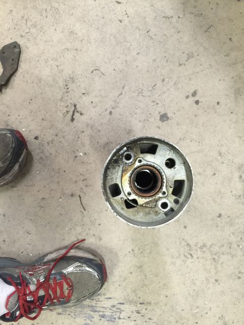1965 Ford Mustang - A wheel hub assembly sits on a concrete floor next to a pair of athletic shoes.