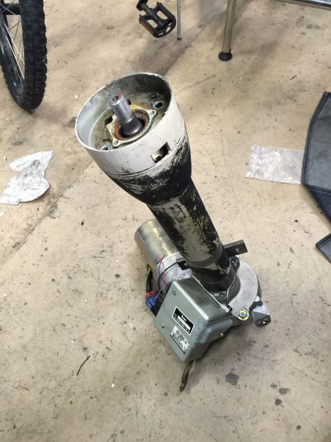 1965 Ford Mustang - A disassembled steering column assembly with an attached motor and visible wiring is shown on a concrete floor.