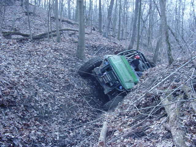 Green off-road vehicle tilted in a ditch on a wooded hillside