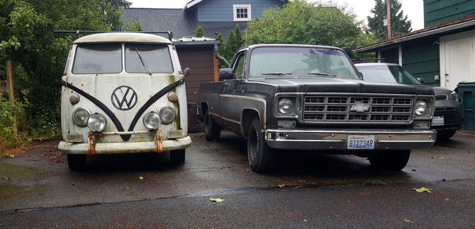 White Volkswagen Type 2 van parked next to a black Chevrolet C/K pickup truck. License plate B72234R