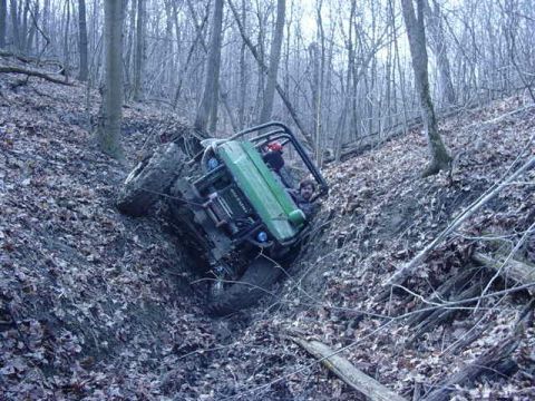 1992 Ford Bronco - An off-road vehicle is stuck on a steep, muddy incline in a wooded area.