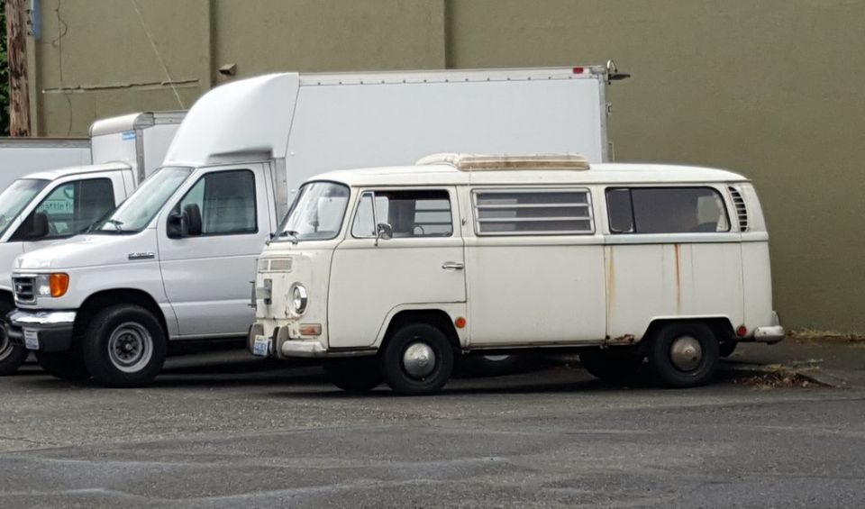 White Volkswagen Type 2 van parked next to a white Ford E-Series van and a box truck