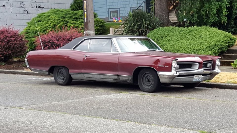 Maroon 1967 Pontiac Grand Prix coupe with black vinyl roof parked curbside