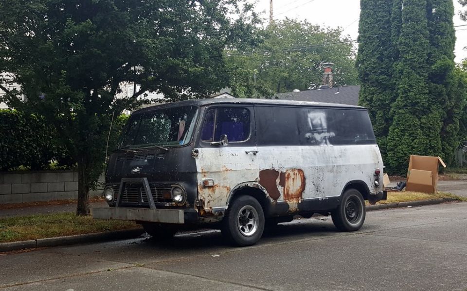 Rusty white and black van with a custom bumper, parked on a street