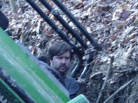 1992 Ford Bronco - A man is visible inside a green vehicle, with dark pipes and foliage in the background.