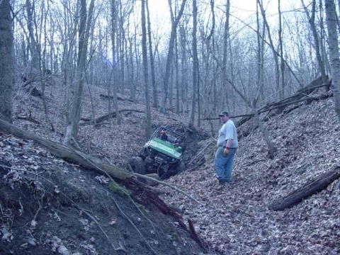 1992 Ford Bronco - A man watches as a green off-road vehicle becomes stuck in a steep, wooded ravine.