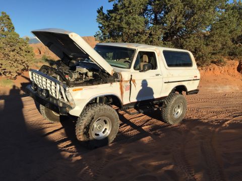 1979 Ford Bronco - White 1978 Ford Bronco with hood open sits on sandy ground in a desert landscape.