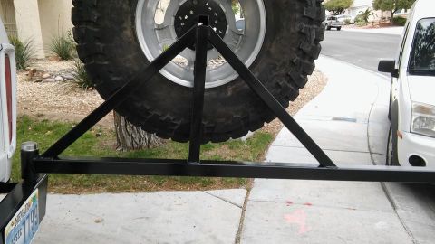 1979 Ford Bronco - A rear-mounted spare tire carrier is shown, attached to the bumper of a vehicle. Another vehicle is visible in the background.