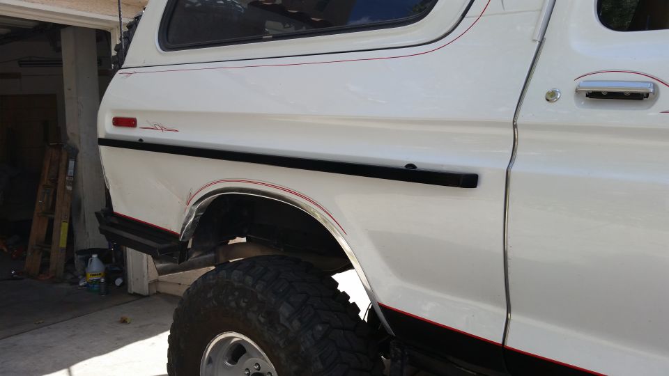 Side view of a white SUV with black trim and red pinstriping. Large off-road tire visible