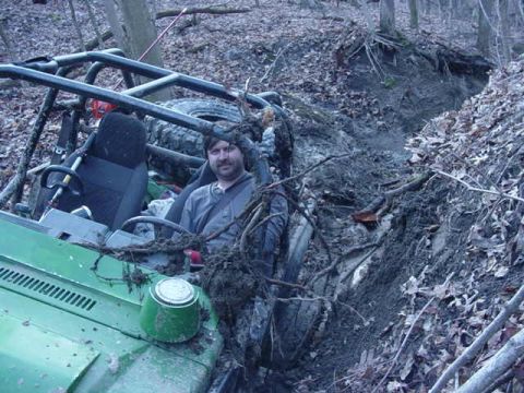 1992 Ford Bronco - This off-road vehicle appears to be stuck in a deep, muddy trench within a wooded area.