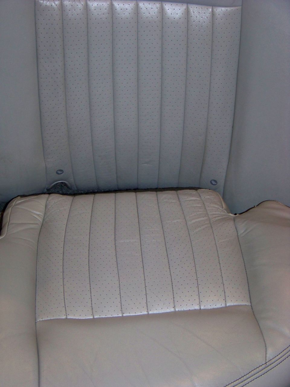 Close-up of light-colored perforated leather car seats, showing the seat bottom and the back of the front seats