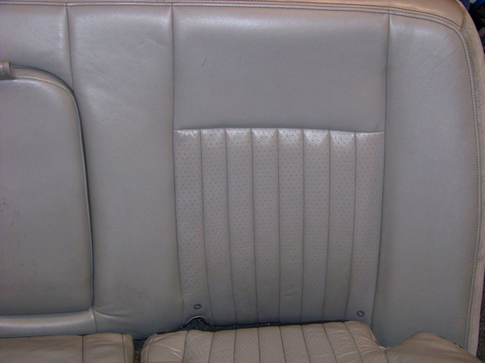 Close-up of a light gray perforated leather rear car seat with stitching detail