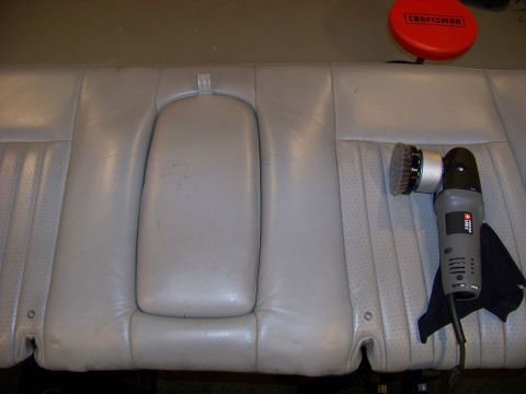 2001 Mercury Grand Marquis - A polishing tool is positioned next to a light gray perforated leather rear car seat, with a red Craftsman buffer visible in the background.