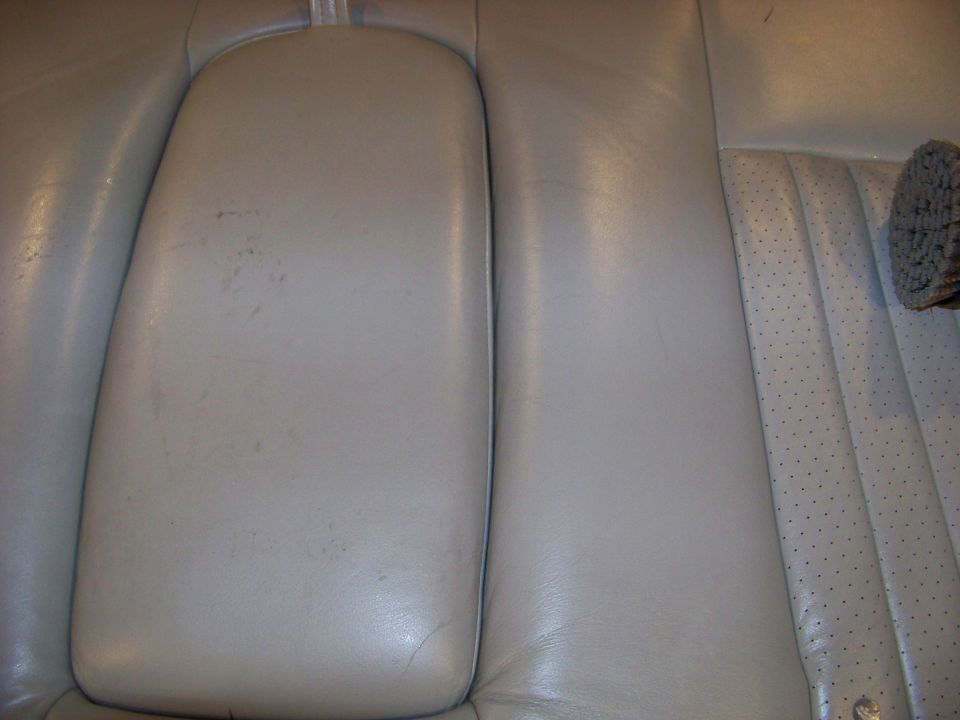 Close-up of light gray leather car seats, showing a center console armrest and perforated seat cushion