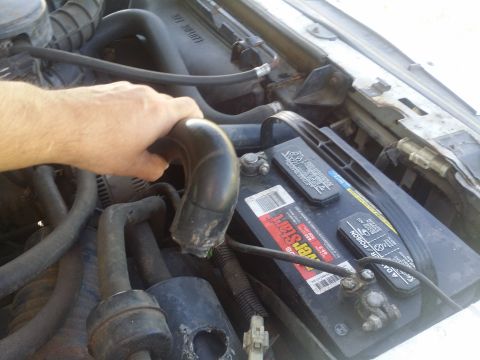1995 Ford Bronco - Close-up of an engine bay with a hand holding a hose near the battery.