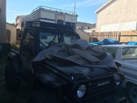 1987 Suzuki Samurai - 1987 Suzuki Samurai with a camper shell on the roof rack, parked next to another vehicle.