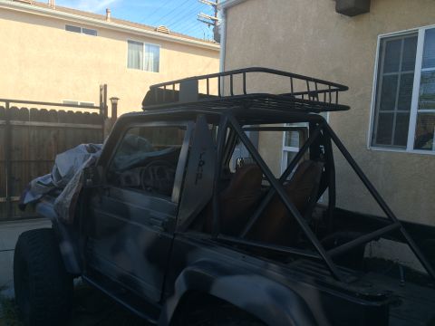 1987 Suzuki Samurai - This Suzuki Samurai has been modified with a roll cage and a roof rack, with the front end partially covered.
