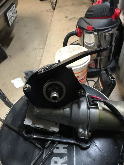 1965 Ford Mustang - A close-up view of a steering column part with attached bracket and wiring, resting on a surface with tools.