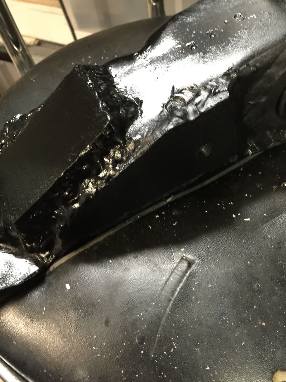 Close-up of a black metal bracket with rough welds. A portion of a black textured surface is visible below