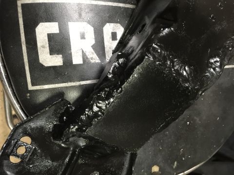 1965 Ford Mustang - A close-up of a black metal bracket shows rough welds and is partially over a surface with white lettering.