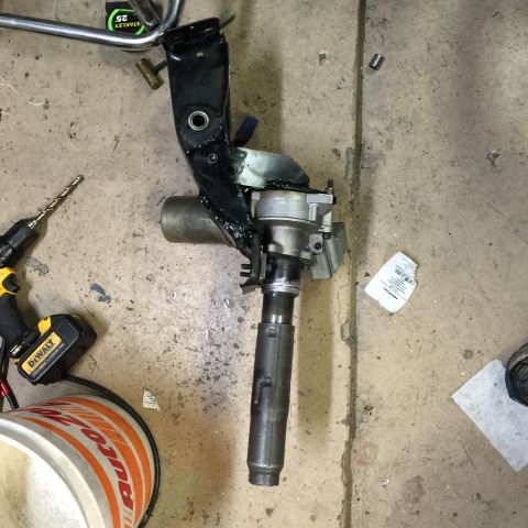 1965 Ford Mustang - Steering column assembly, likely from a vehicle, shown disassembled on a workshop floor.