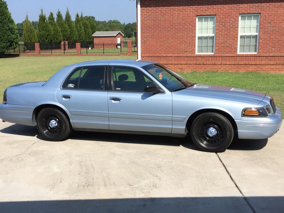 Light blue sedan parked on concrete driveway, side view. Black steel wheels, tinted windows