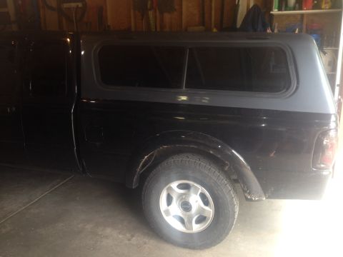 2001 Ford Ranger - A black pickup truck with a grey camper shell is parked in a garage.