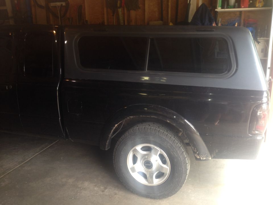Side view of black pickup truck with grey camper shell