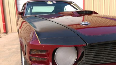 1970 Ford Mustang - A custom 1970 Ford Mustang with a prominent hood scoop and racing stripes is parked in front of a garage door.